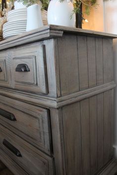 an old dresser with white dishes on top and pine branches in the backgroung