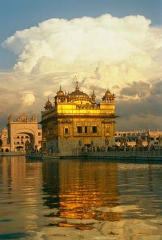 the golden building is reflected in the water near other white buildings and blue sky with clouds