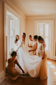 a group of women standing next to each other in front of a window wearing dresses