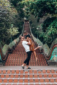 a man and woman are dancing on the steps in front of some green trees,