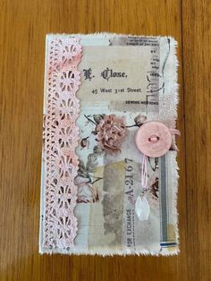 an altered piece of fabric with lace and buttons on it, sitting on top of a wooden table