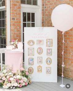 a pink and white table with balloons, flowers and pictures on the wall next to it