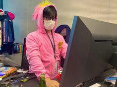 a person wearing a pink bunny costume standing in front of a computer with a face mask on