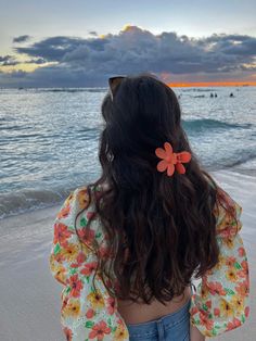 a woman standing on top of a beach next to the ocean with a flower in her hair