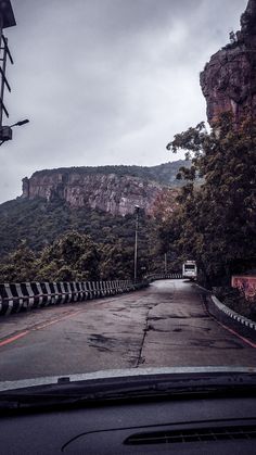 an empty road with mountains in the background and trees on both sides, as seen from inside a car