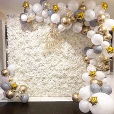 an arch made out of balloons and gold stars on the wall is decorated with white, silver and gold balls