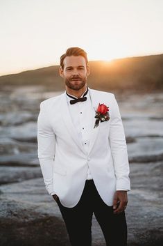 a man in a white tuxedo with a red rose boutonniere