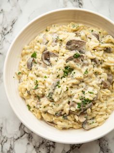 a bowl filled with pasta and mushrooms on top of a marble countertop next to a fork