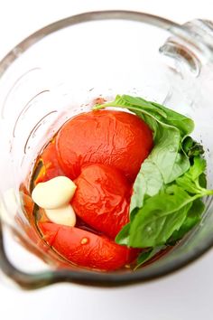 tomatoes and spinach in a blender on a white surface with some green leaves