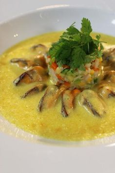 a white bowl filled with soup and garnished with parsley on top, sitting on a table