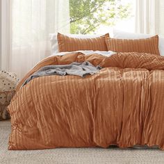 a bed with an orange comforter and two pillows on top of it in front of a window