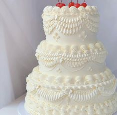 a three tiered white wedding cake with cherries on top and ruffles