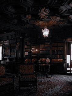 a dark room with chairs, tables and bookshelves on the walls is lit by a chandelier