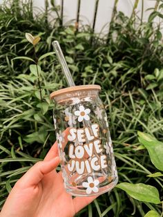 someone holding up a glass with the words self love juice on it in front of some plants