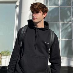 a young man wearing a black hoodie standing in front of a white building with windows