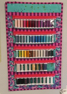 a wall hanging with many different colored threads on it's sides and an assortment of spools in the middle