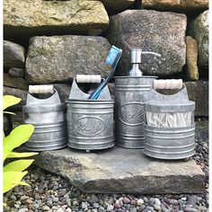 three metal canisters with toothbrushes in them are sitting on some rocks