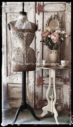 an old fashion mannequin is next to a small table with flowers on it