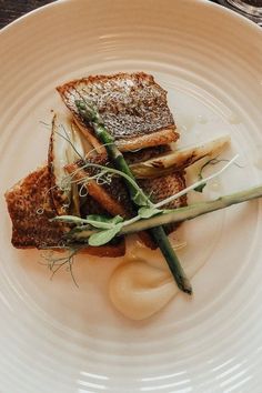 a white plate topped with fish and asparagus on top of a wooden table