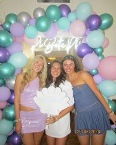 three women standing in front of a balloon arch