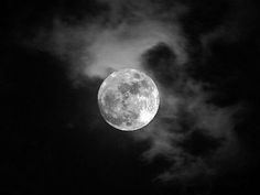 the full moon is seen through clouds in black and white