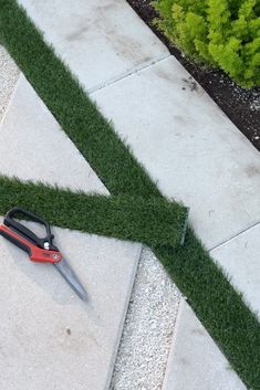 a pair of scissors laying on top of grass next to a green tape that has been cut into the shape of an arrow