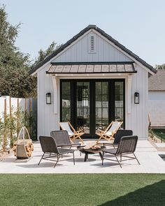 a patio with chairs and a table in front of a white building that has a black door