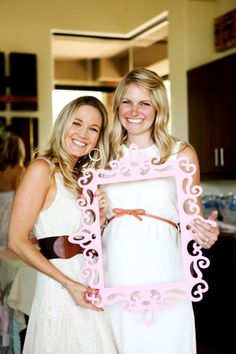 two women standing next to each other holding a pink frame