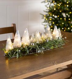 a wooden table topped with christmas trees and white lights next to a small pine tree