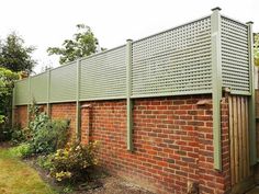 a brick building with a green metal fence on it's side next to a garden