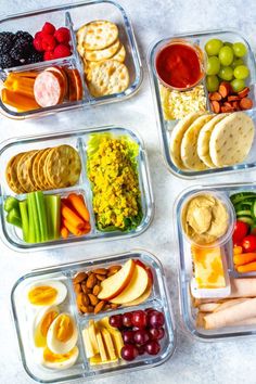 four plastic containers filled with different types of food including crackers, fruit and vegetables