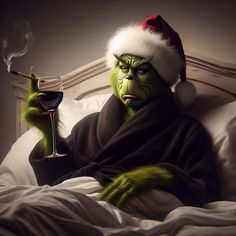 a man in a santa claus hat holding a glass of wine while sitting on a bed