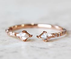 a rose gold ring with two small white stones on it, sitting on a marble surface