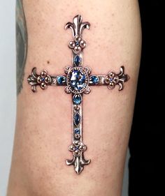 a cross tattoo with blue stones on it