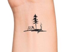 a tattoo on the wrist of a woman with a tree and tent in the background