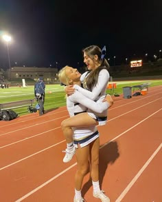 two cheerleaders hugging each other on a track