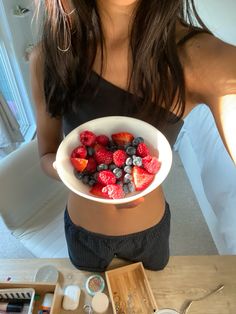 a woman holding a bowl full of berries and strawberries