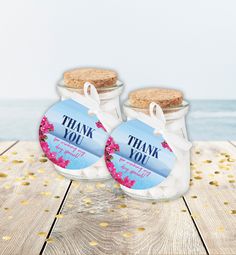 two glass jars with thank you labels on them sitting on a wooden table next to the ocean