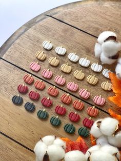 several pairs of colorful earrings sitting on top of a wooden table next to cotton balls