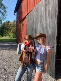 two women standing next to each other in front of a red barn wearing cowboy hats