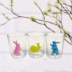 three glasses with different designs on them sitting next to a tree branch and brick wall