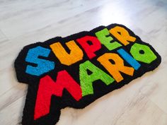 a rug with the words super mario on it sitting on a wooden floor in front of a white wall