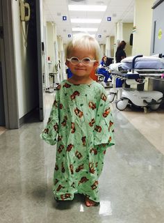 a little boy wearing glasses standing in a hospital hallway