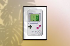 a nintendo gameboy cross stitch pattern hanging on a wall next to a potted plant