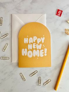 a card with the words happy new home on it next to pencils and paper clips