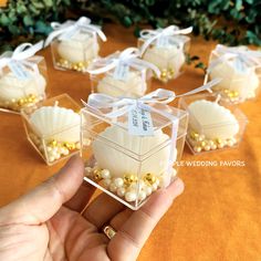 a hand holding a small box filled with white chocolate covered in gold and white pearls