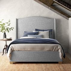 a bed sitting in a bedroom next to a wooden table and plant on top of it