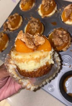 a person holding up a cupcake in a muffin tin filled with desserts