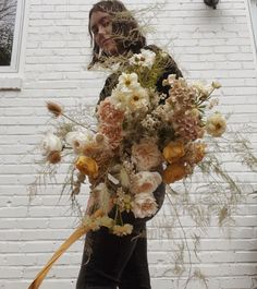 a woman holding a bouquet of flowers in front of a white brick building