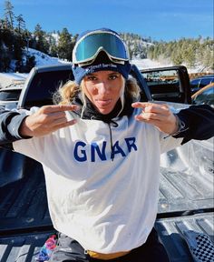 a woman with goggles on sitting in the bed of a truck and pointing to the camera